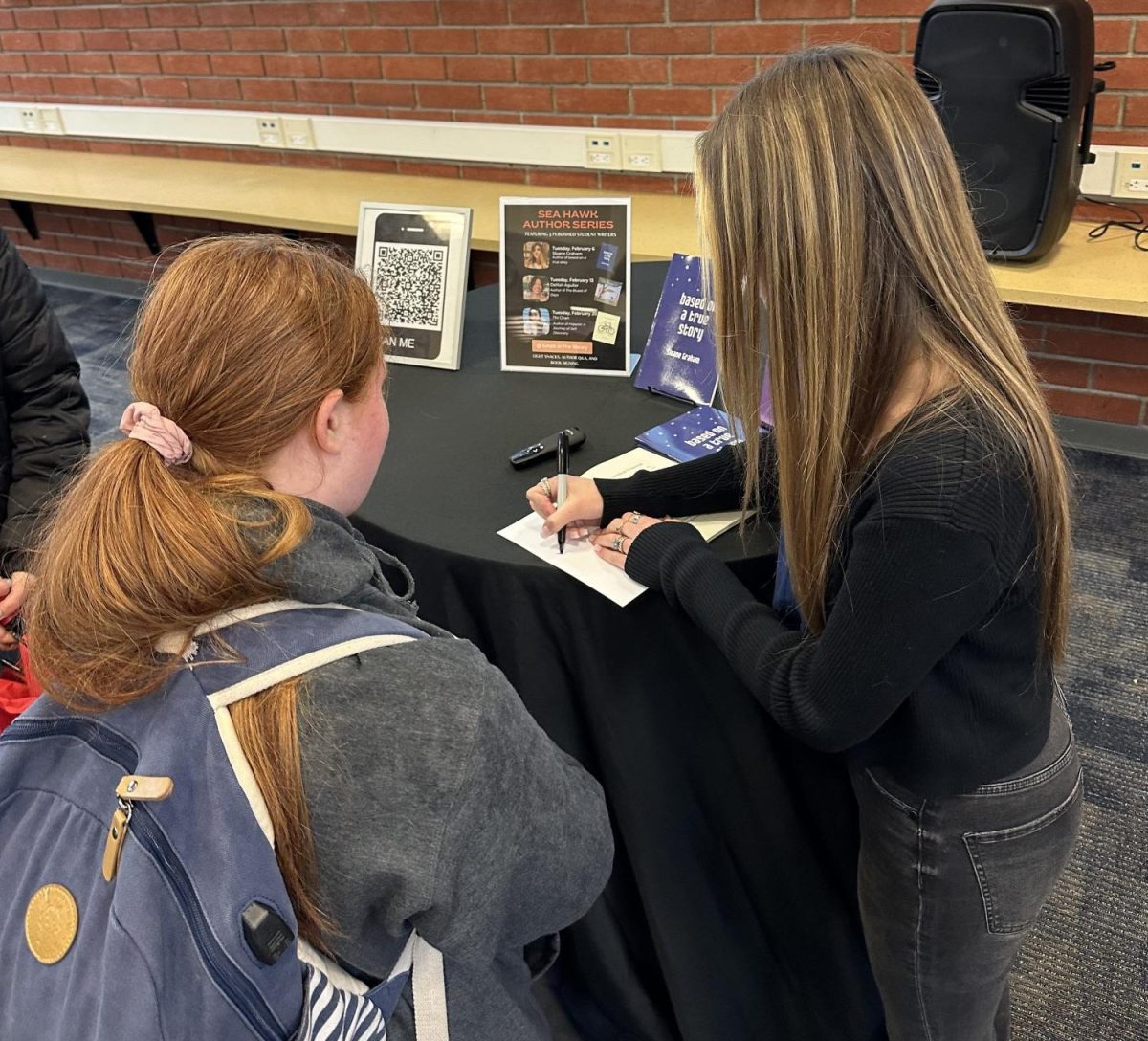 Junior Sloane Graham signs a copy of her book for a fellow student. 